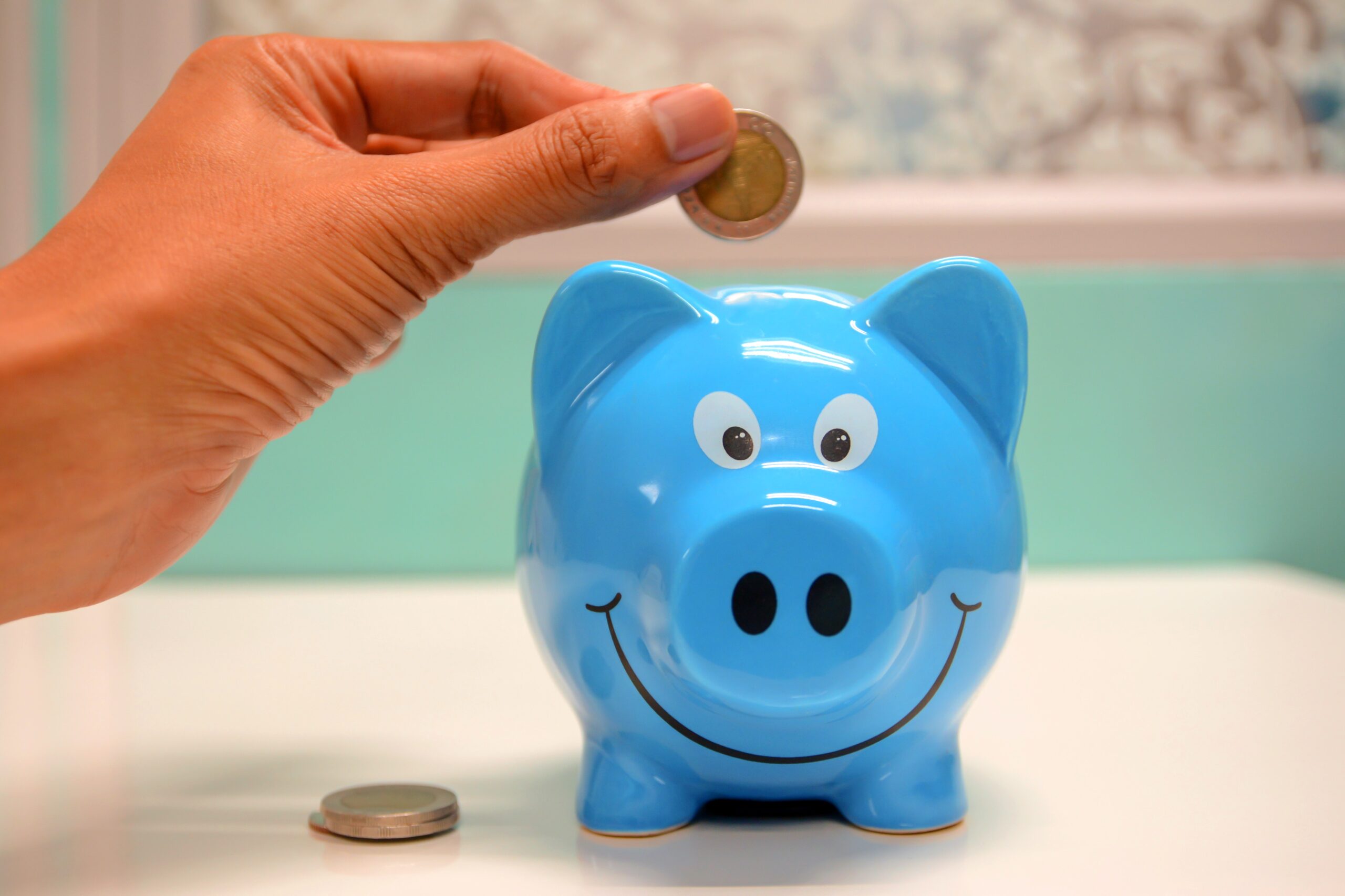 A hand is dropping a coin into a blue piggy bank